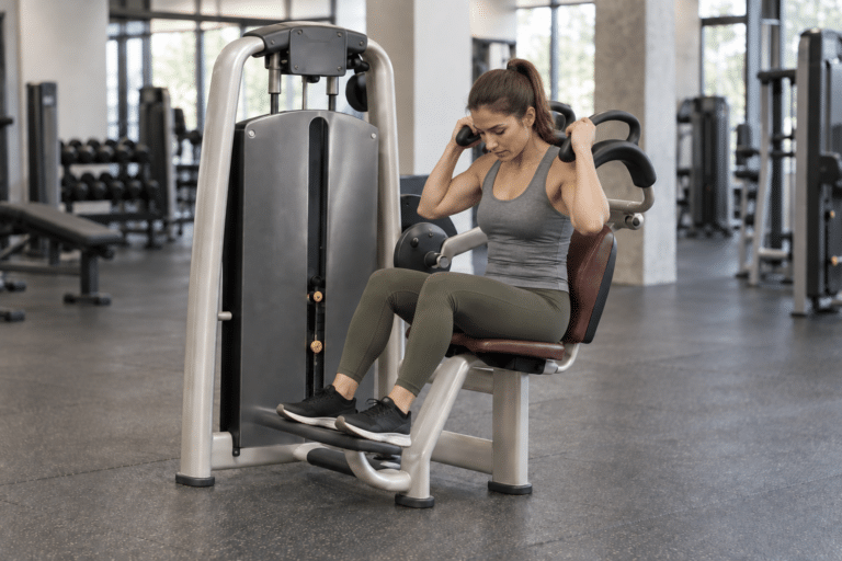Femme assise sur une machine à crunch abdominal, les mains sur les poignées hautes.